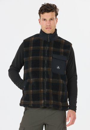 Man draagt een zwart en bruin geruit fleecevest met een rits aan de voorkant en borstzak over een zwart shirt met lange mouwen en groene broek.