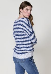 Maglione a strisce bianco e blu scuro, realizzato in filato soffice. Vestibilità ampia con scollo largo e orlo a coste. Abbinato a jeans blu con ricami floreali.