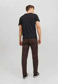 Schwarzes T-Shirt mit kurzen Ärmeln und rundem Halsausschnitt, kombiniert mit braunen Slim-Fit-Hosen und schwarzen Sneakers mit weißen Akzenten, von hinten betrachtet.