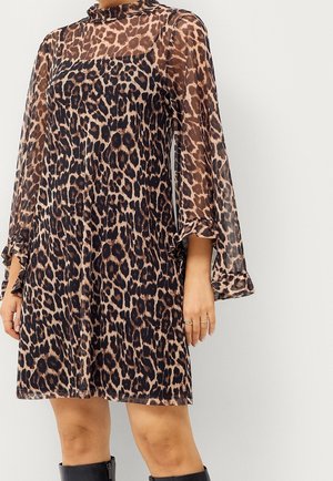 Vrouw met een jurk met luipaardprint, doorschijnende lange mouwen en ruches aan de manchetten, gecombineerd met zwarte kniehoge laarzen.