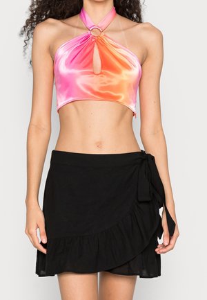 Frau trägt ein pink-orangefarbenes, in einem Farbverlauf gehaltenes Neckholder-Bauchfreies Oberteil mit Ausschnitt und einen schwarzen, gerafften Wickelrock, der an der Taille gebunden ist.