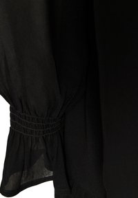 Μαύρο διάφανο ύφασμα μανίκι με ελαστικό ριγωτό μανσέτα που δημιουργεί πτυχώσεις και μια ελαφριά φούστα στον καρπό.