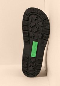 Suela de zapato de goma negra con fuertes surcos, superficie texturizada y una etiqueta verde que dice "El Naturalista."