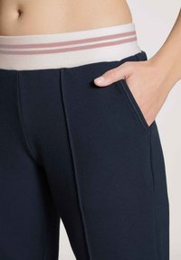 Marineblauwe trainingsbroek met een witte tailleband en roze strepen. Zakken aan de zijkant en een gladde, zachte stofstructuur.