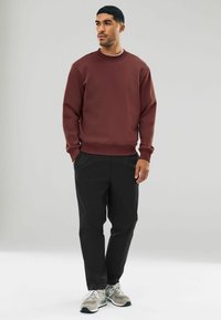 Hanorac bordo cu guler rotund și manșete cu nervuri, purtat cu pantaloni negri tapered și teniși gri. Textură netedă, design casual.