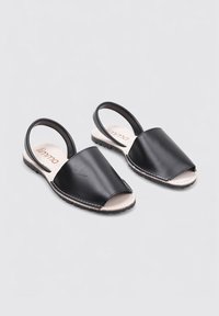 Sandalias slingback de cuero negro con diseño de punta abierta, plantilla beige en contraste y suela de goma texturizada. Presenta un borde cosido.