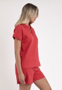 Camisa polo roja de manga corta, con cuello y corte recto, combinada con pantalones cortos rojos a juego. Textura suave y diseño sencillo.