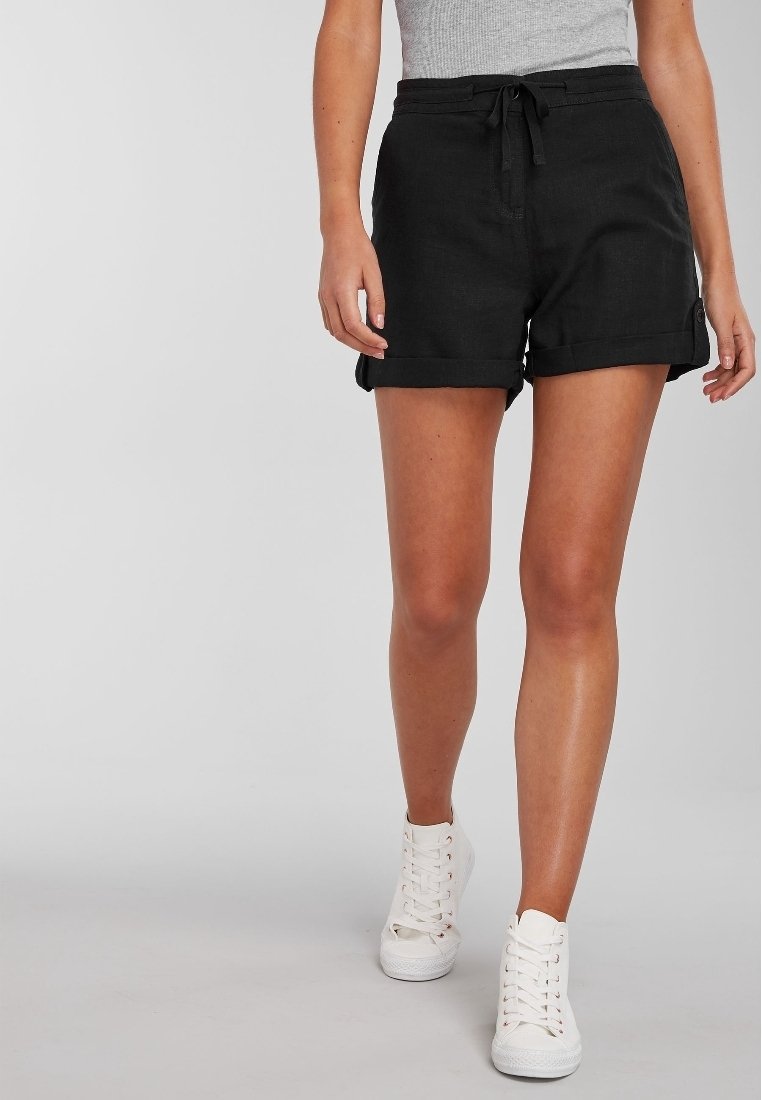 Pantaloni corti neri in lino con vita regolabile, orli arrotolati e tasche laterali, abbinati a sneakers bianche alte.