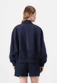 Ναυτική τζάκετ μπομπέρ με ψηλό γιακά, ριχτές μανσέτες και στρίφωμα. Διαθέτει χαλαρή και άνετη εφαρμογή καθώς και λεία, ελαφριά υφή.