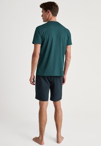Donker teal T-shirt met korte mouwen gecombineerd met donkere shorts. Het T-shirt heeft een ronde halslijn; de shorts hebben een elastische tailleband en een zachte textuur.