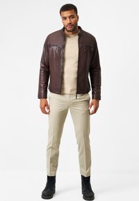 Brun läderjacka med dragkedjefickor, beige tröja, krämfärgade byxor och svarta snörskor. Slät textur och figurnära design.