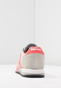 Zapatilla de ante gris con acentos rosas, que presenta un logo en el talón, un collar acolchado y una suela con tracción.