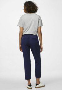 Pelēks T-krekls ar īsām piedurknēm, apvienots ar tumši ziliem biksēm ar elastīgu jostu un divām aizmugurējām kabatām. Baltas un melnas sporta kurpes.