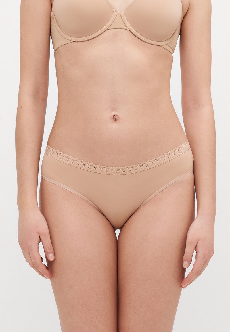 Nude hipster undertøy med en bølget elastisk midje, glatt tekstur og minimalistisk design.