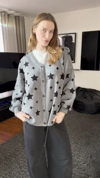 Šedý kardigan s černým vzorem hvězd, s výstřihem do V, zapínáním na knoflíky a žebrovanými manžetami. Nošený se černými kalhotami s širokými nohavicemi.