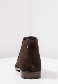Bottes Chelsea en daim marron avec panneaux latéraux élastiques, semelle texturée et petit accent tricolore au talon. Finition lisse avec bout arrondi.