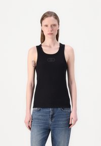 Schwarzes, geripptes Tanktop mit Rundhalsausschnitt und breiten Trägern, das in der Mitte ein dezentes Logo-Detail aufweist. Kombiniert mit blauen Jeans.