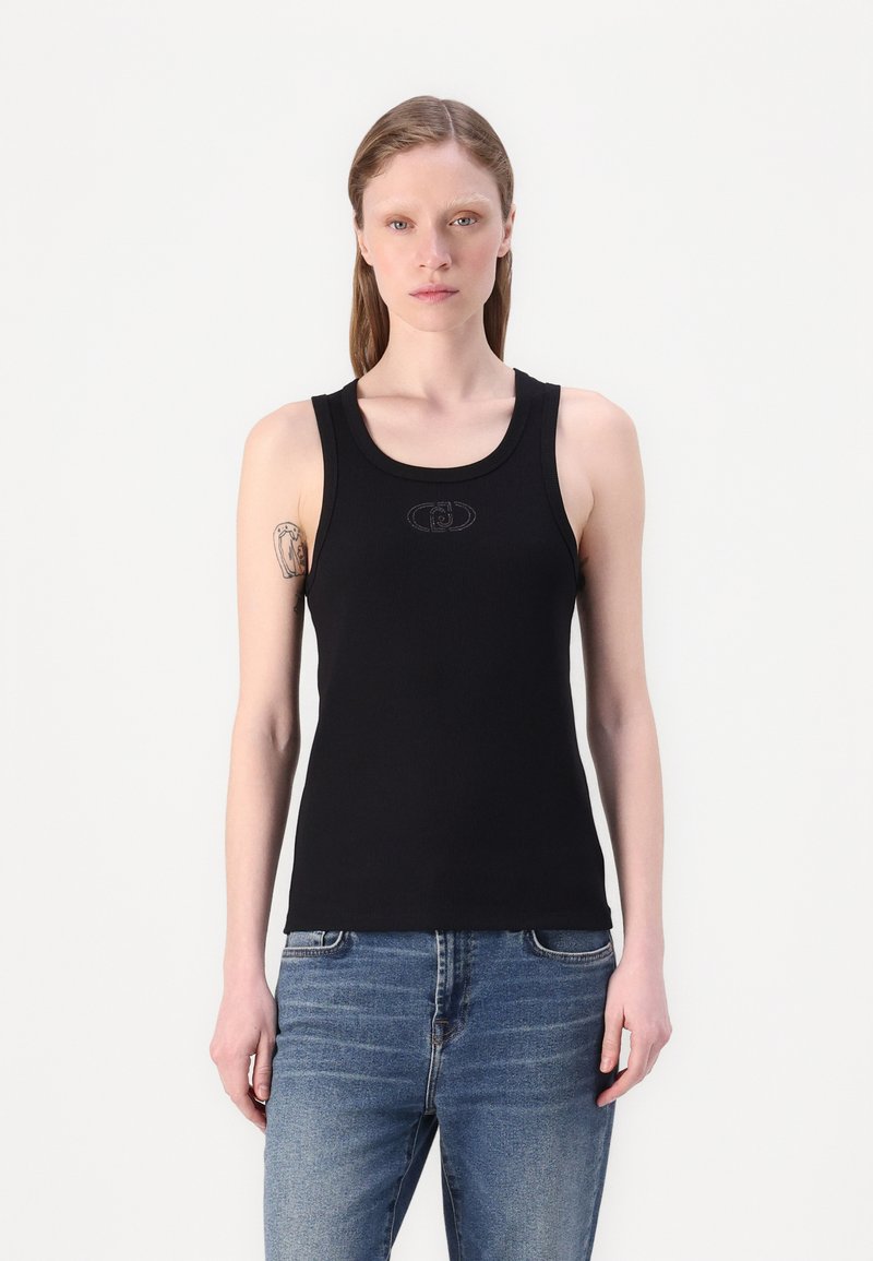 Schwarzes, geripptes Tanktop mit Rundhalsausschnitt und breiten Trägern, das in der Mitte ein dezentes Logo-Detail aufweist. Kombiniert mit blauen Jeans.