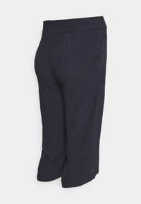 Calças cropped azul marinho com um cós elástico, apresentando uma textura suave e forma afunilada. O material leve cai suavemente.