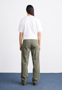 Olivgröna byxor med rak passform och bakfickor, kombinerat med en enkel vit t-shirt med kort ärm. Slät textur och avslappnad design.