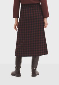 Gonna a scacchi in rosso scuro e blu navy, realizzata in tessuto testurizzato. Presenta una vita elastica, lunghezza fino al polpaccio, abbinata a stivali al ginocchio.