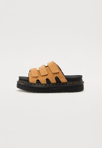 Le ciabatte in suede color sabbia presentano tre cinturini regolabili, una suola in gomma nera con un battistrada testurizzato e un'etichetta di cucitura gialla a contrasto.