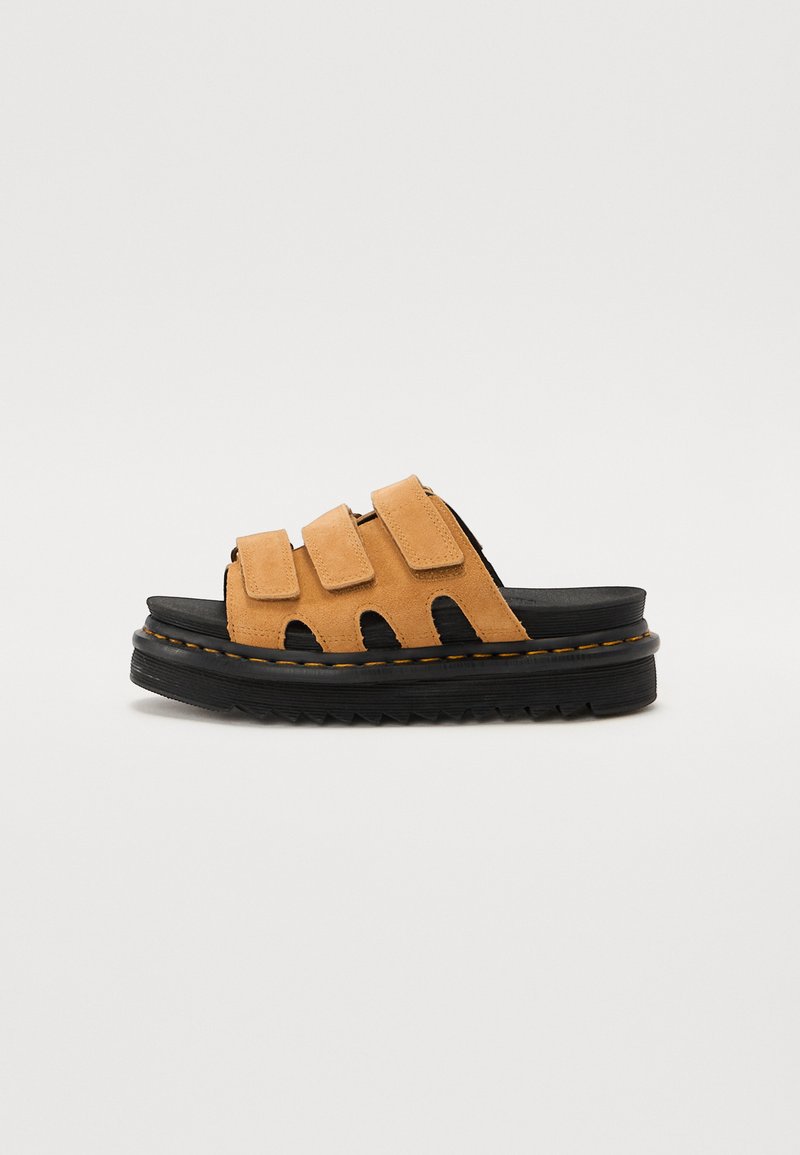 Le ciabatte in suede color sabbia presentano tre cinturini regolabili, una suola in gomma nera con un battistrada testurizzato e un'etichetta di cucitura gialla a contrasto.