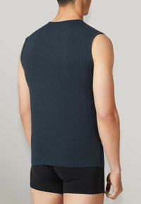 Canotta blu navy senza maniche in cotone, con scollatura rotonda e design aderente, indossata con pantaloni corti neri, vista da dietro.