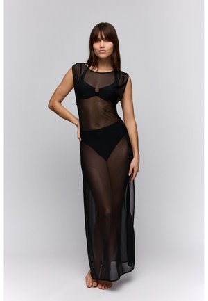 Zwarte doorschijnende maxi-jurk met korte mouwen, voorzien van een ronde halslijn en een centraal cirkelaccent. De jurk heeft een losse pasvorm en valt tot aan de enkels.
