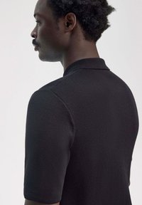 Polo shirt nero a manica corta con tessuto textured, caratterizzato da un colletto classico e un design slanciato, mostrato da un'angolazione laterale.