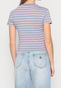 Camiseta de rayas en azul claro y rosa, de manga corta, con un diseño ajustado. Se lleva con unos vaqueros de cintura alta de denim claro que presentan un parche con logo.