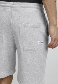 Shorts de sport gris en tissu doux, dotés d'une poche arrière et d'une petite étiquette de marque. Design décontracté avec une taille élastique.