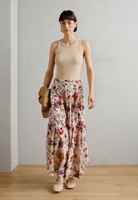 Canotta beige abbinata a una gonna maxi a fiori a strati con fiori rossi e blu su uno sfondo chiaro, indossata con delle scarpe basse beige e una borsa marrone.