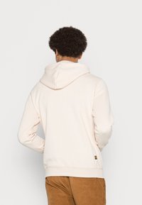Hoodie bege claro com um bolso canguru, capuz com cordão e punhos canelados. Tecido suave com uma textura lisa. Design simples, sem padrões.