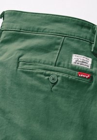 Poche arrière verte d’un pantalon Levi's avec fermeture par bouton et étiquettes de marque Levi's blanches et rouges cousues au-dessus de la poche.