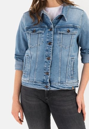 Hellblaues Jeansjacke mit Knopfleiste, zwei Brustklappentaschen und hochgekrempelten Ärmeln, getragen über einem weißen Hemd mit dunklen Jeans.