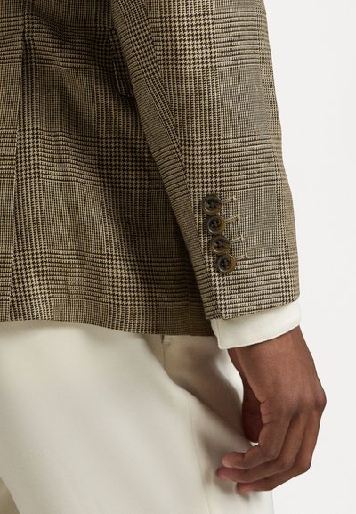 Sacou cu carouri maro și bej, dintr-un material texturat, cu patru nasturi negri pe manșetă și o cămașă albă care iese de sub acesta.