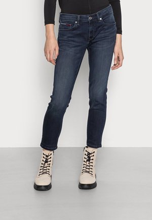 Jeans de mezclilla azul oscuro con un corte slim, diseño de cinco bolsillos y costuras visibles; combinados con botas beige con cordones.