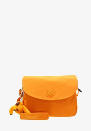 Sac bandoulière orange vif avec rabat à l’avant, logo circulaire embossé, sangle ajustable et petit porte-clés singe en peluche attaché.