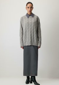 Pelēks, adīts džemperis ar plašu, ribotu apakšmalu, uzvilkts virs garas tumši pelēkas svārku. Spīdīgi melni potīšu zābaki noslēdz apģērbu.