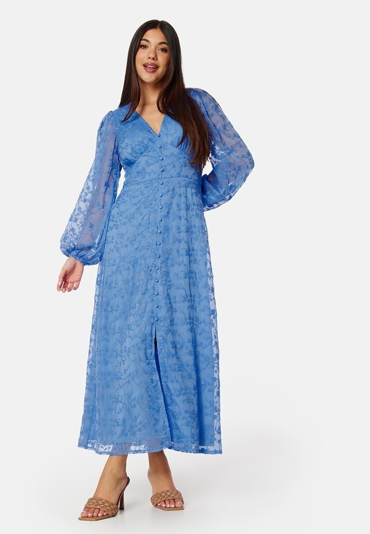 Lång blå klänning i genomskinligt tyg med blommönsterbroderi, långa puffärmar och knäppning fram, med en slits i botten.