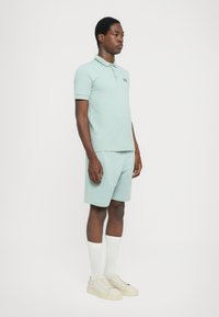 Polo verde menta com mangas curtas e colarinho, combinado com calções a condizer. Completado com meias brancas acima do joelho e ténis bege.