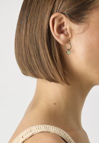 Gold hoop earrings with a small heart charm, featuring a smooth finish and a delicate design, worn on an ear by a person with short hair.