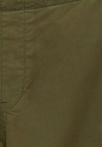 Gros plan sur un tissu vert olive avec des lignes de couture visibles et des détails de couture sur le côté gauche.