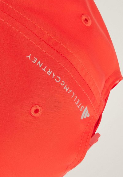 Gorra de color naranja brillante, hecha de tela suave con costuras blancas. Presenta un logo y agujeros de ventilación, diseñada para uso casual.