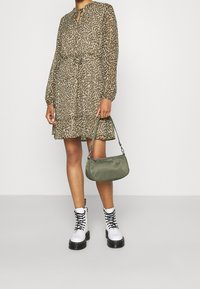 Klänning med leopardsmönster och långa ärmar, nyckelhålsdetalj vid halsen, indragen midja; tillsammans med en olivgrön handväska och vita snörstövlar.