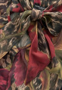 Foulard en soie à motifs floraux dans des tons riches de rouge, vert et marron. Texture légère et transparente avec un joli détail de nœud.