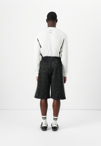 Top alb cu mâneci lungi și accente negre, completat cu pantaloni scurți negri asortați, având un model cu imprimeu leopard. Modelul poartă pantofi negri și șosete albe.