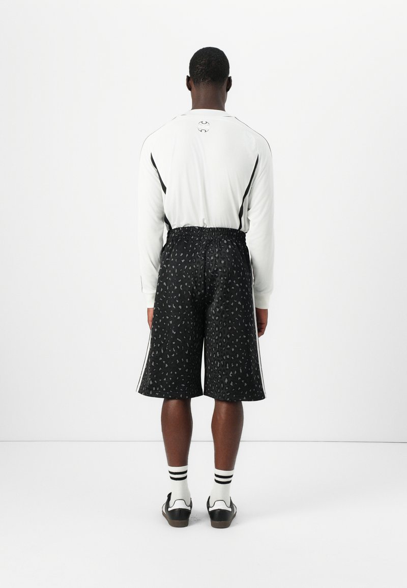 Długi rękaw biały top z czarnymi akcentami i dopasowane czarne szorty z wzorem w panterkę. Model nosi czarne buty i białe skarpetki.