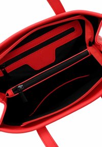 Interno di una borsa in pelle rossa con fodera nera, numerosi scomparti con zip e un logo impresso su una tasca. Texture liscia in tutto.